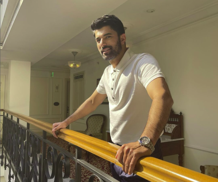 Engin Akyurek in an indoor setting, smiling happily on a balcony 