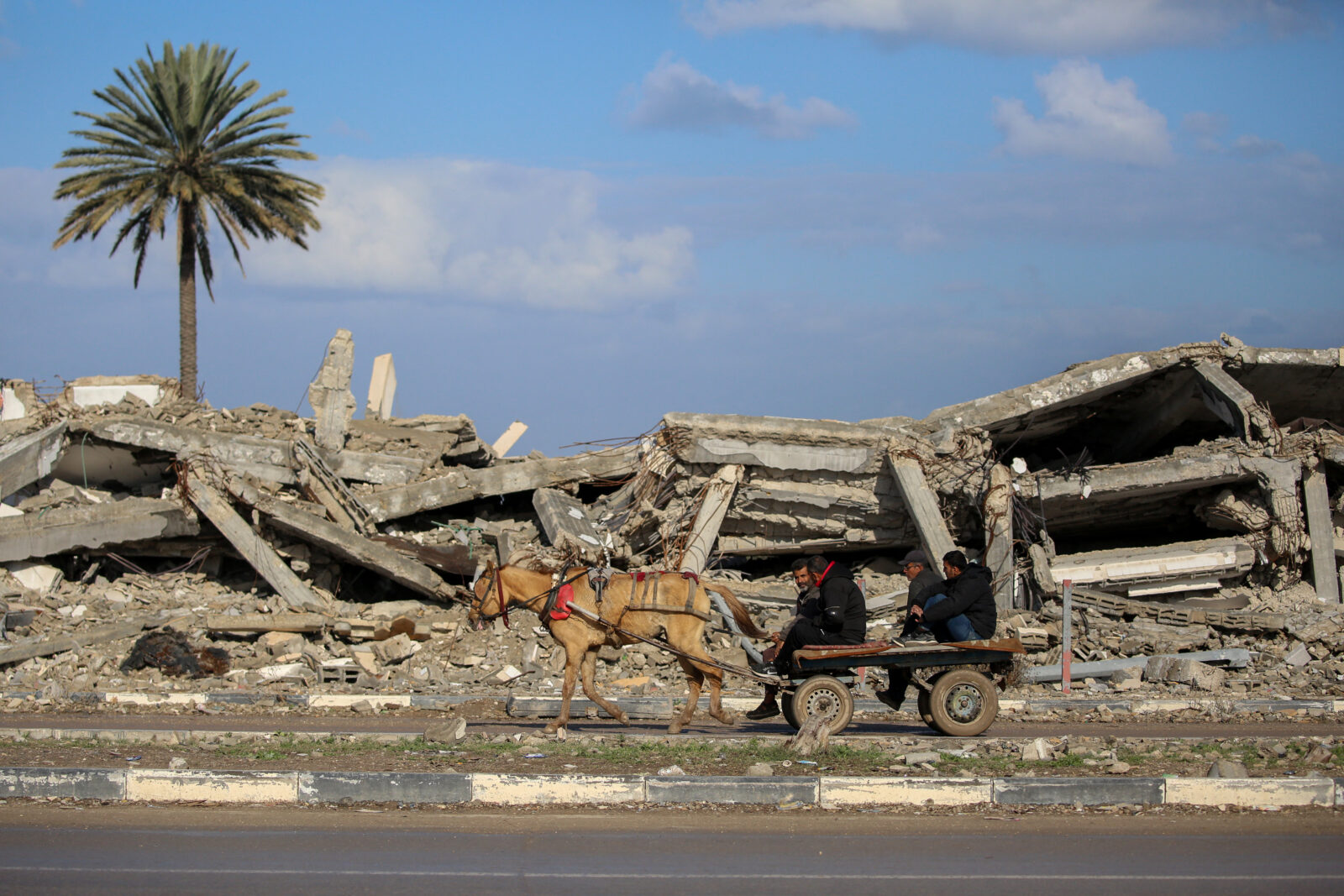 Civilians ride an animal pulled cart past the rubble of a destroyed building