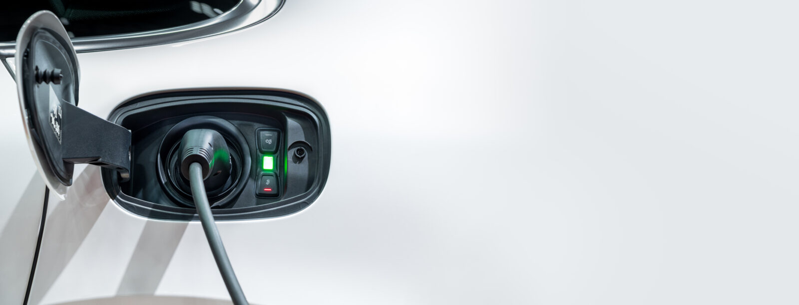 A close-up of an EV charging port with a plugged-in cable and a glowing green indicator light.