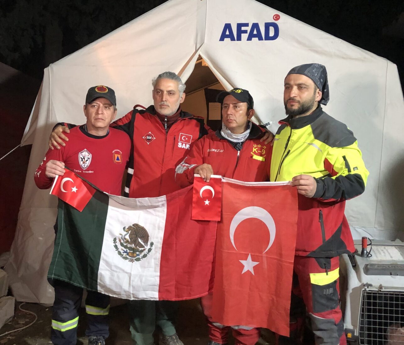 Mexican and Turkish SAR members hold their national flags in front of an AFAD tent during rescue efforts