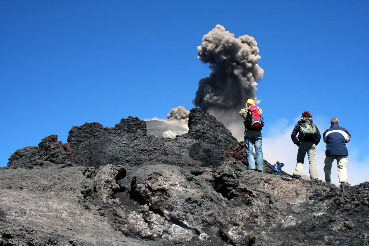 Tourist group of three near Mount Etna while ash eruptions happen.