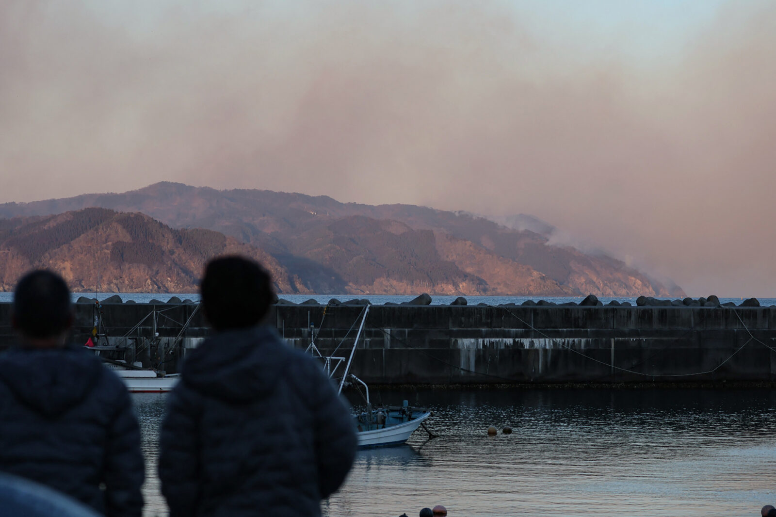 Photo shows People look out at smoke rising from a forest fire near the city of Ofunato