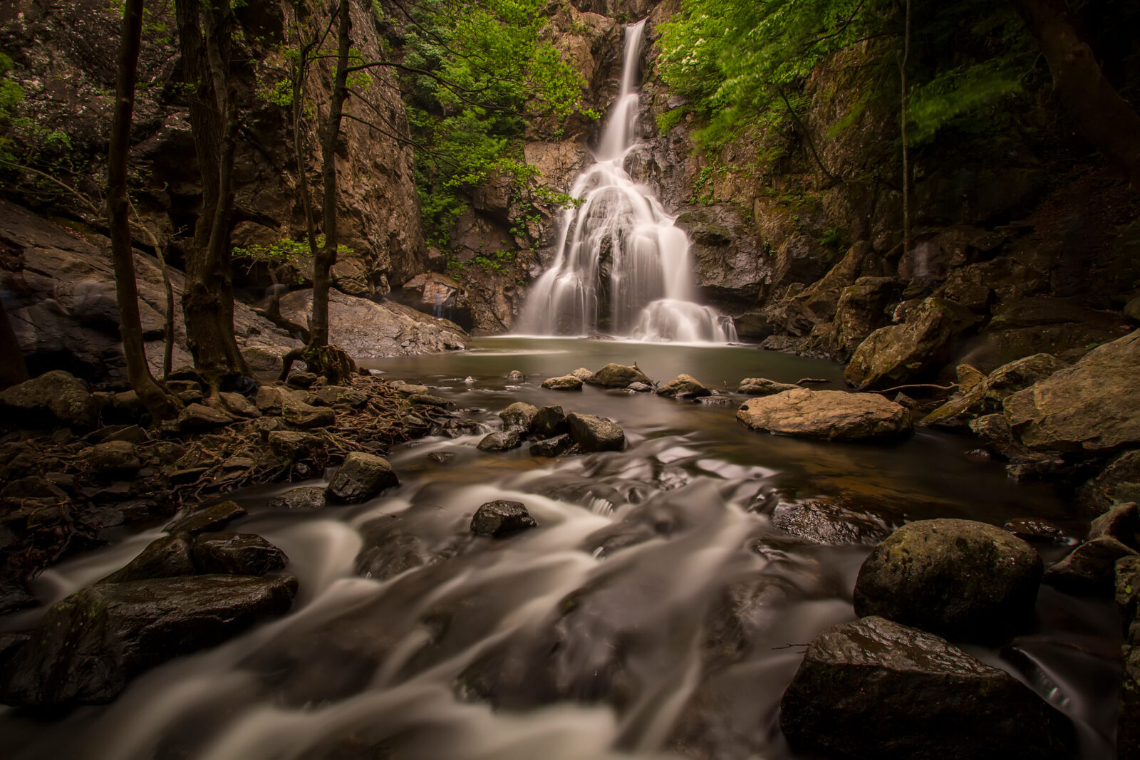 A scenic view of Erikli Waterfall in Yalova province, surrounded by dense green forests and rocky terrain, with a flowing stream in the foreground.