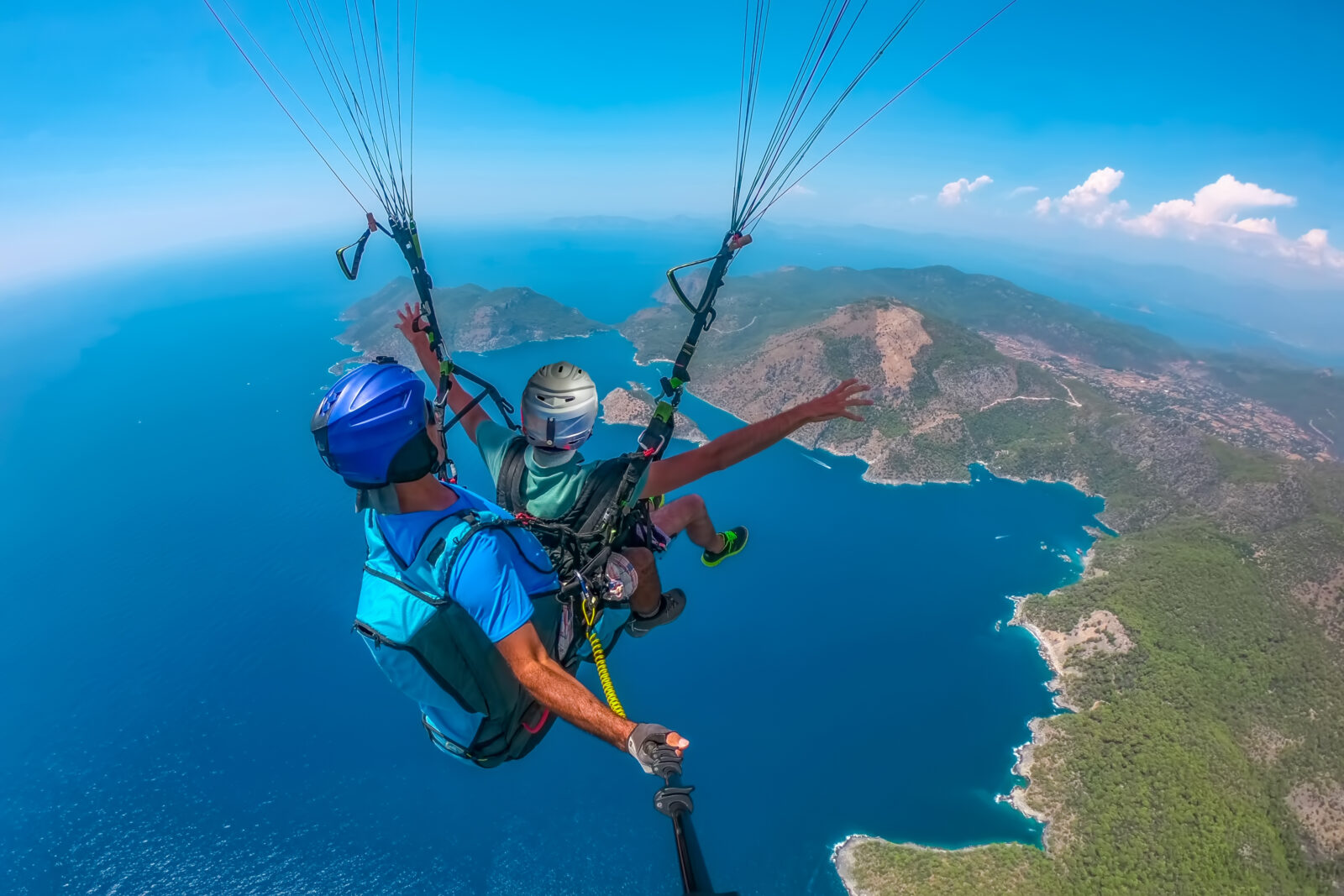 Paraglider flying over the sea with blue water and mountains in bright sunny day.