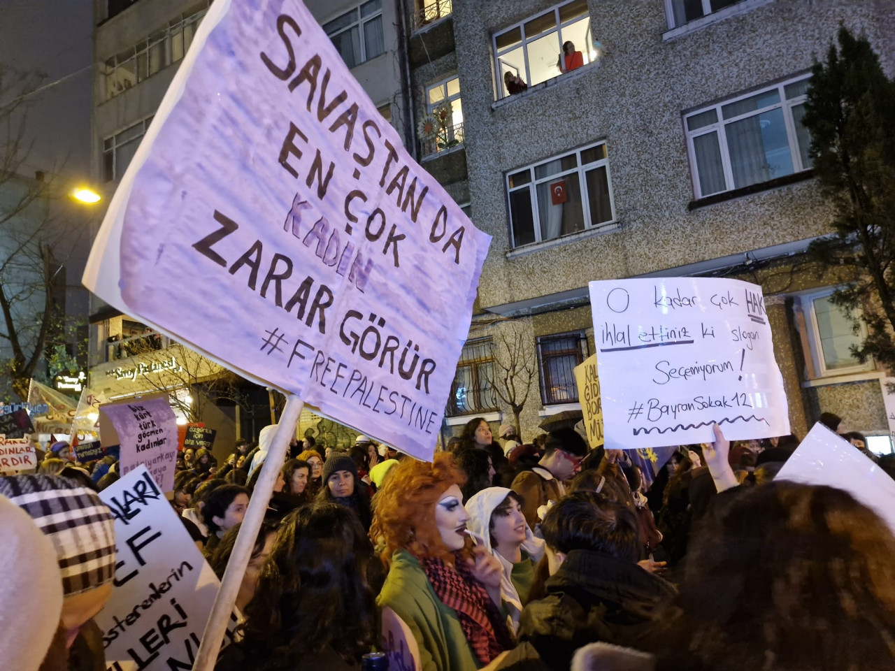 A woman holds a banner at the Feminist Night March, highlighting the disproportionate impact of war on women and showing solidarity with Palestine.