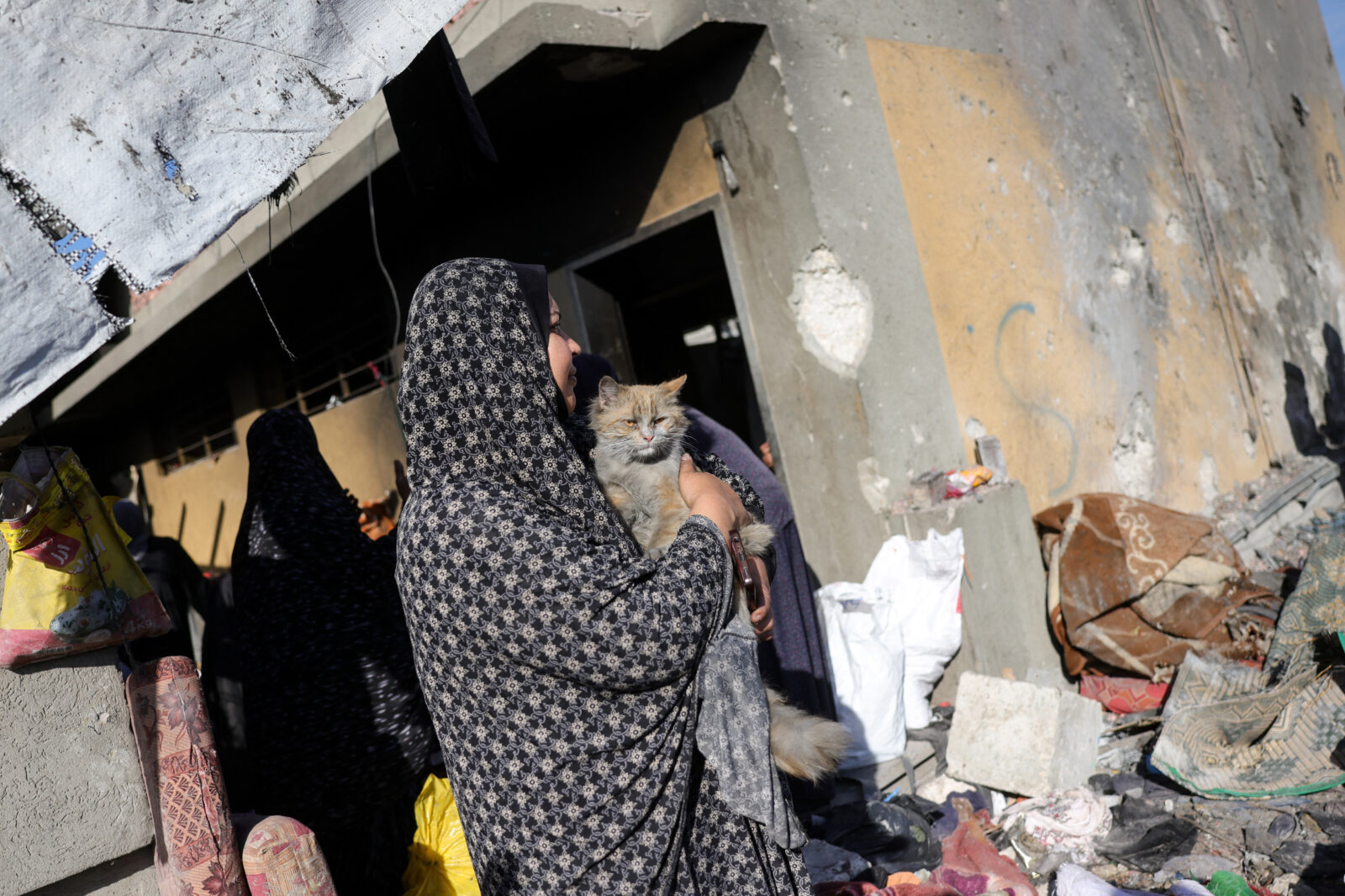 A Palestinian woman holding a cat stands amid the destruction following an Israeli strike that hit a school-turned-shelter