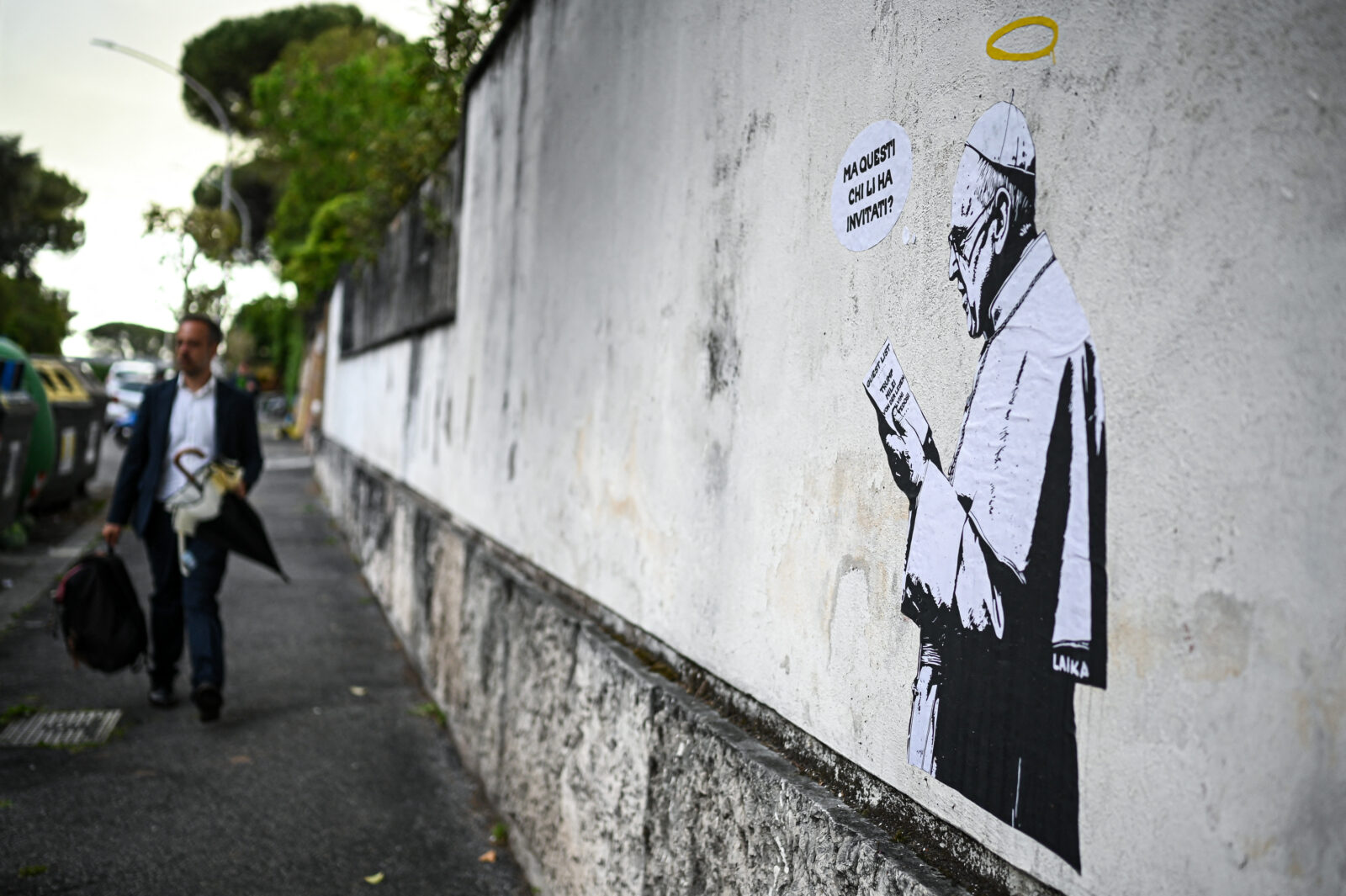Street art depicts Pope Francis reading a paper with a list of leaders (Trump, Milei, Von der Leyen) and a text bubble 