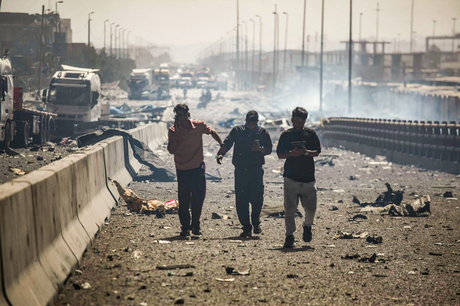 Photo shows people using their telephones as they walk along a devastated boulevard following an explosion.