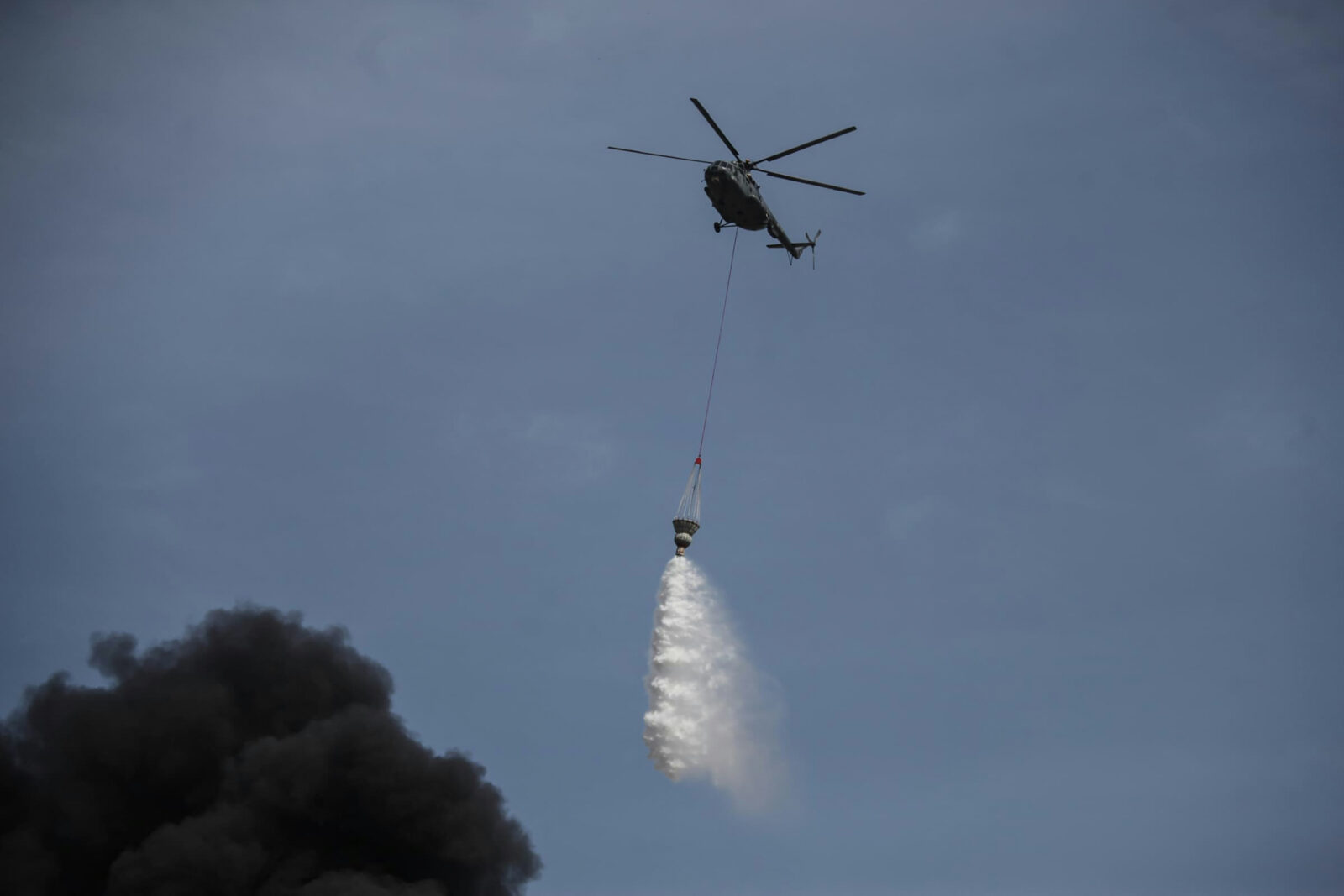 A helicopter drops water over the flames following an explosion at the Shahid Rajaee port dock southwest of Bandar Abbas in the Iranian province of Hormozgan